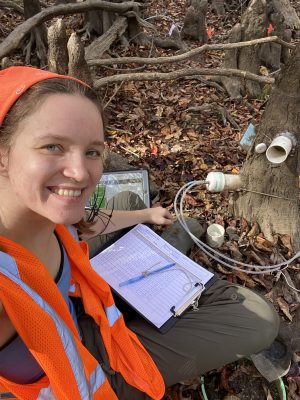 Skylar Ross, sitting with a clipboard in the forest.